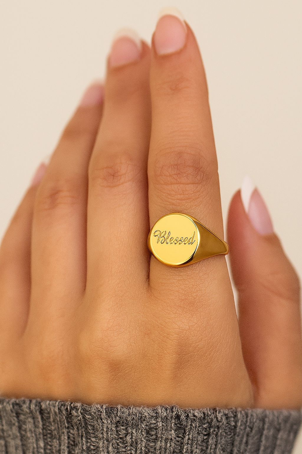 Gold ring with 'Blessed' engraving on a hand against a neutral background