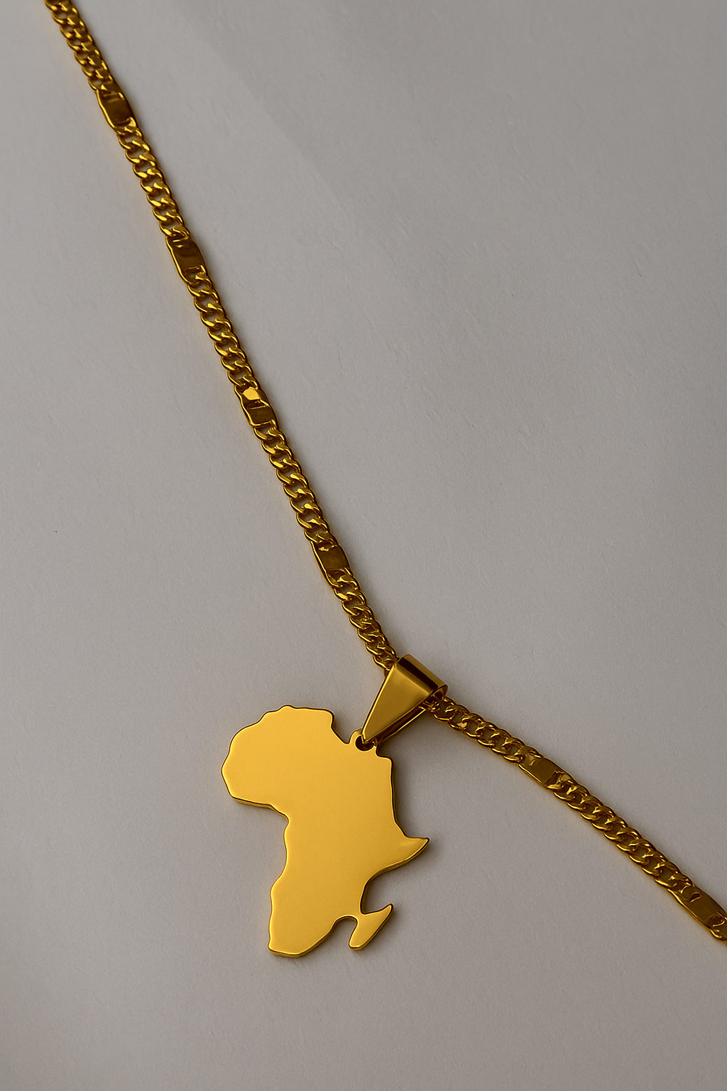 Gold necklace with a pendant shaped like the African continent on a gray background